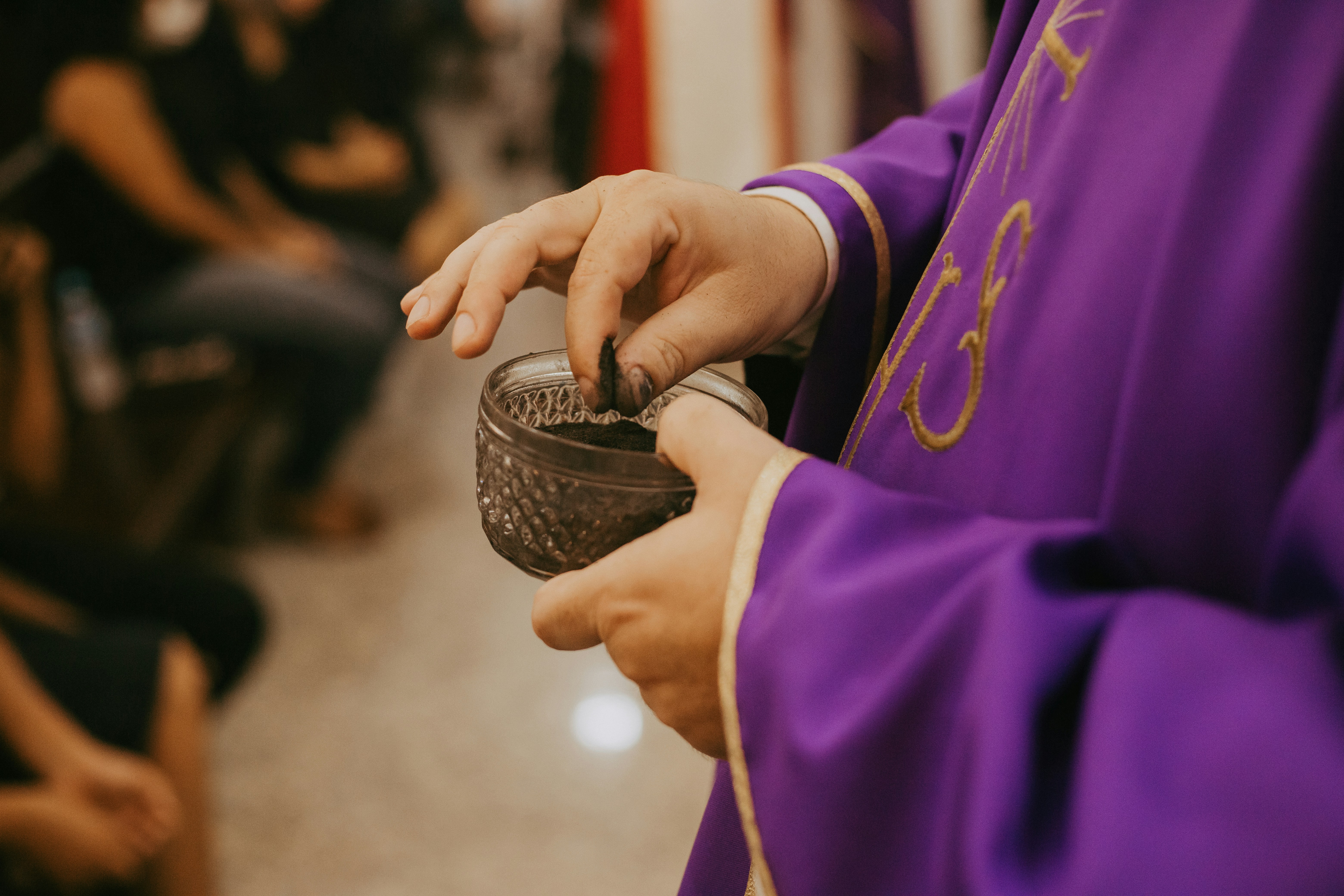 A priest in purple vestments holding a bowl of ash 